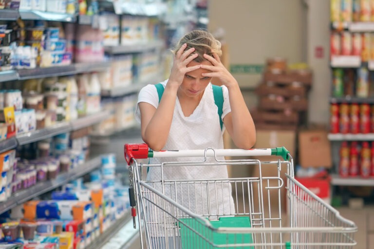 mental toll of gluten free diet woman is sitting with head in hands with an empty shopping cart