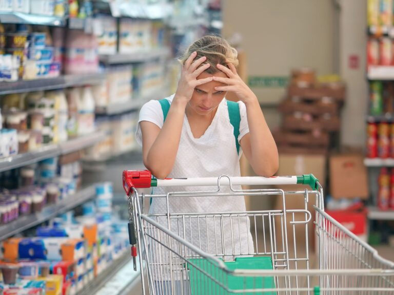 mental toll of gluten free diet woman is sitting with head in hands with an empty shopping cart