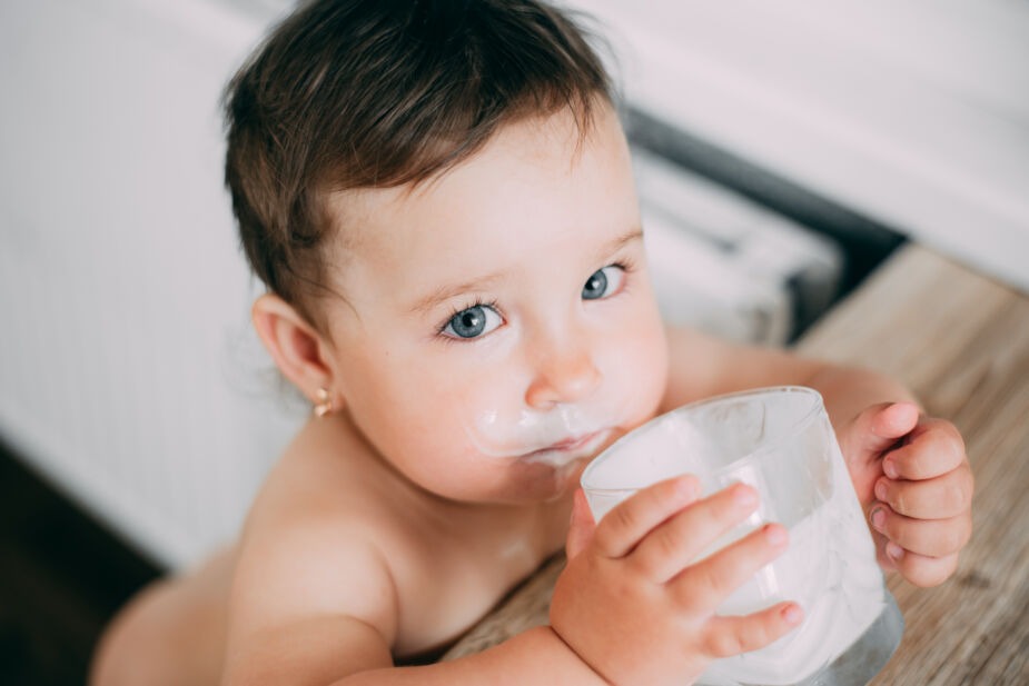 what is a2 milk and should babies drink it? Image of toddler with dark hair and blue eyes drinking a cup of milk