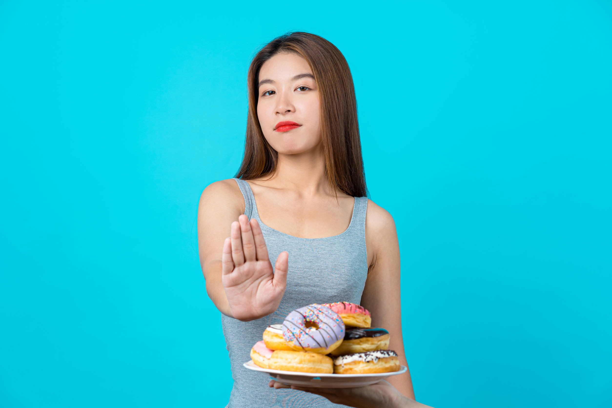 Woman on a sucrose intolerance diet putting her hand out to say no to donuts. She is on a low sucrose diet