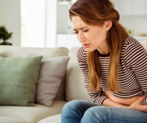 woman sitting on couch holding her stomach in pain