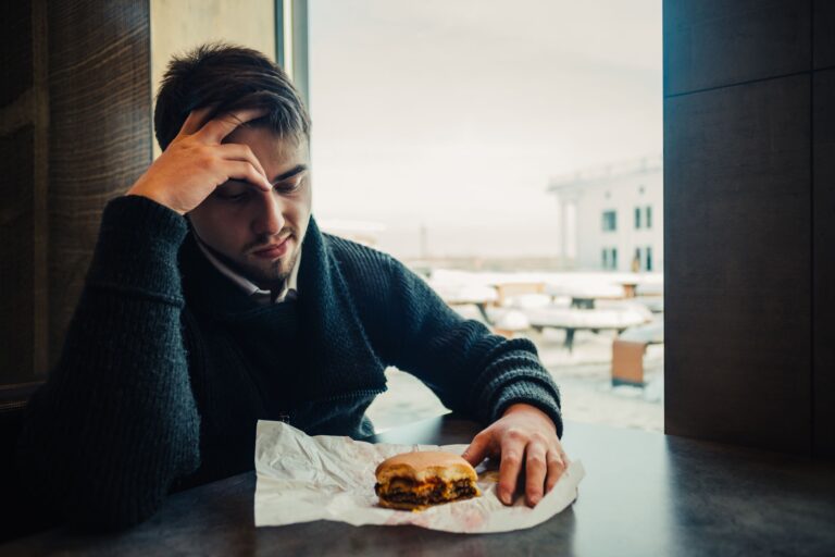 A man looking unwell due to a new food intolerance after he has had gastroenteritis, a stomach infection. He is looking at a sandwich looking ill