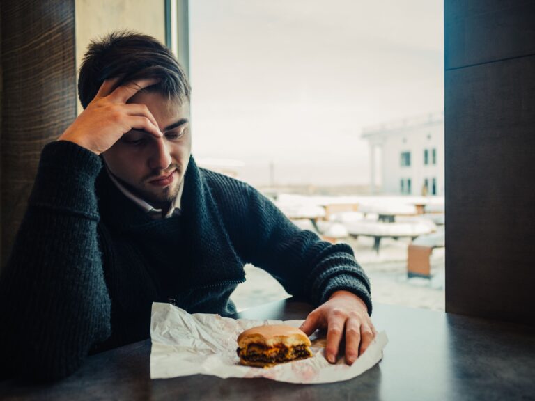 A man looking unwell due to a new food intolerance after he has had gastroenteritis, a stomach infection. He is looking at a sandwich looking ill