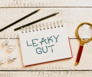 Image is words leaky gut on a notepad with a magnifying glass. A leaky gut diet differs depending on who you talke to