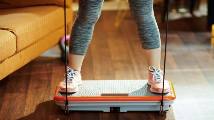 Woman standing on a whole body vibration plate to do exercise and experience whole body vibration therapy and vibration plate benefits. Warable vibration devices have benefits too