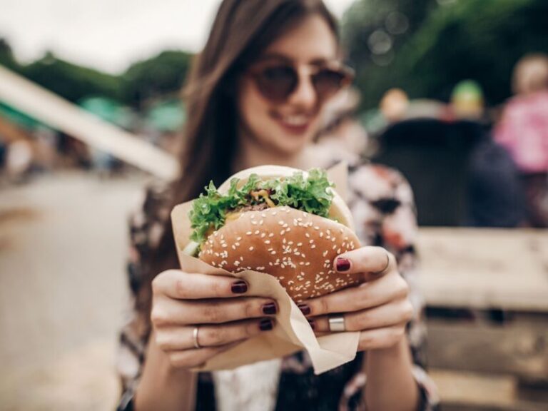 alpha gal symptoms start after a tick bite and then eating meat. Image is of a young woman holding a burger