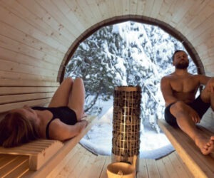 Two people inside a Barrel Sauna with a large window that looks upon the forest. Barrel sauna health benefits are many