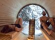 two adults in a barrel sauna with a view window to the forest.