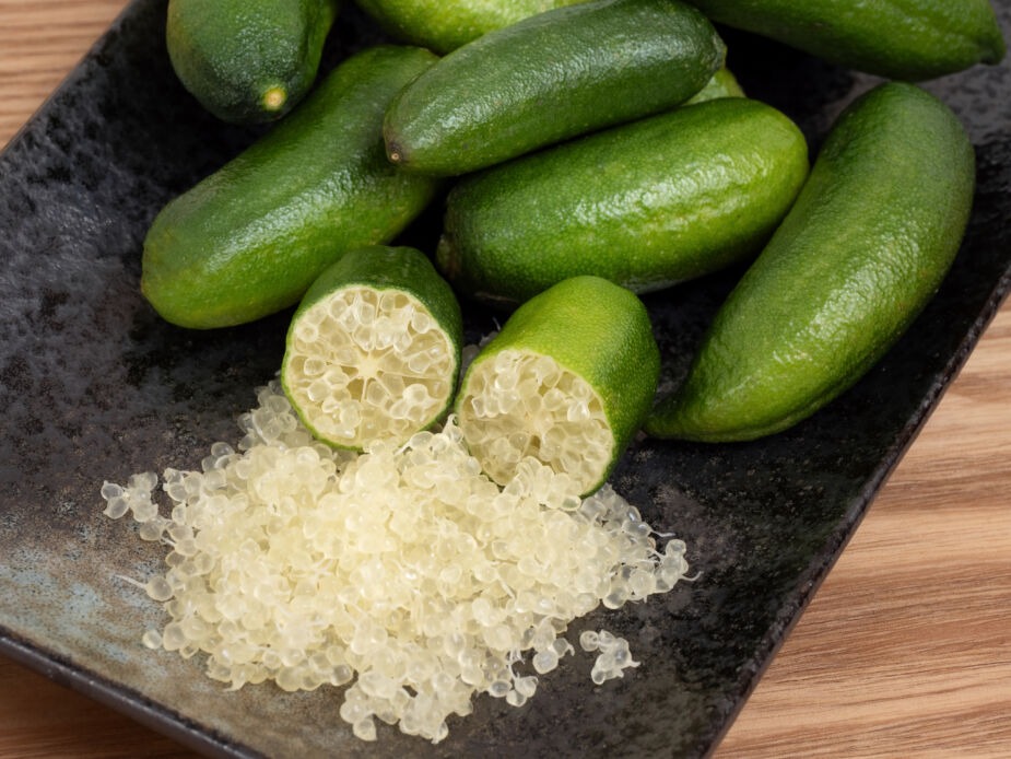 finger limes on a black plate with the inside white pearls of the finger lime spilling out